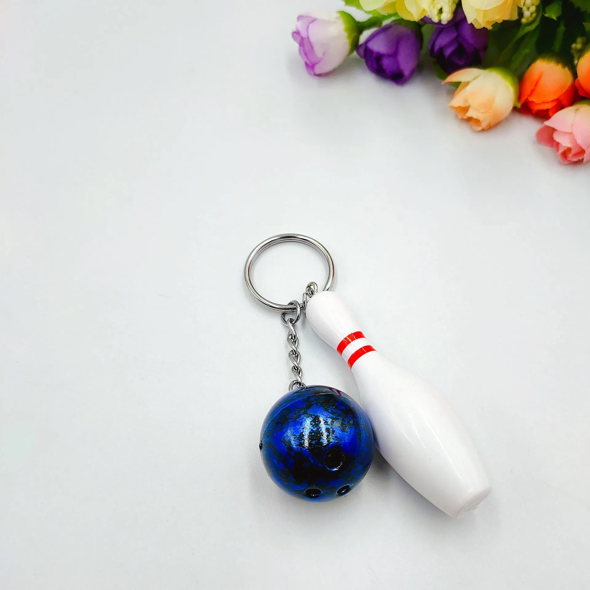 Miniature dark red bowling ball keychain on a metal key ring against a white background.